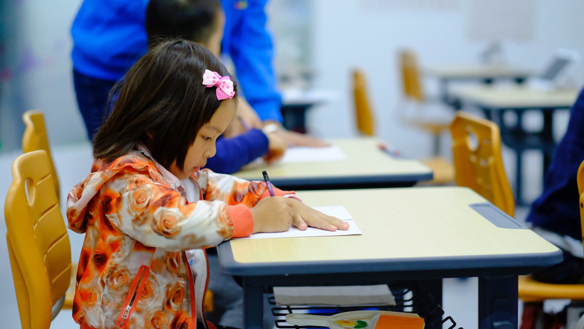 Aluna do Colégio Jaguaré escrevendo em uma mesa laranja da sala de aula
