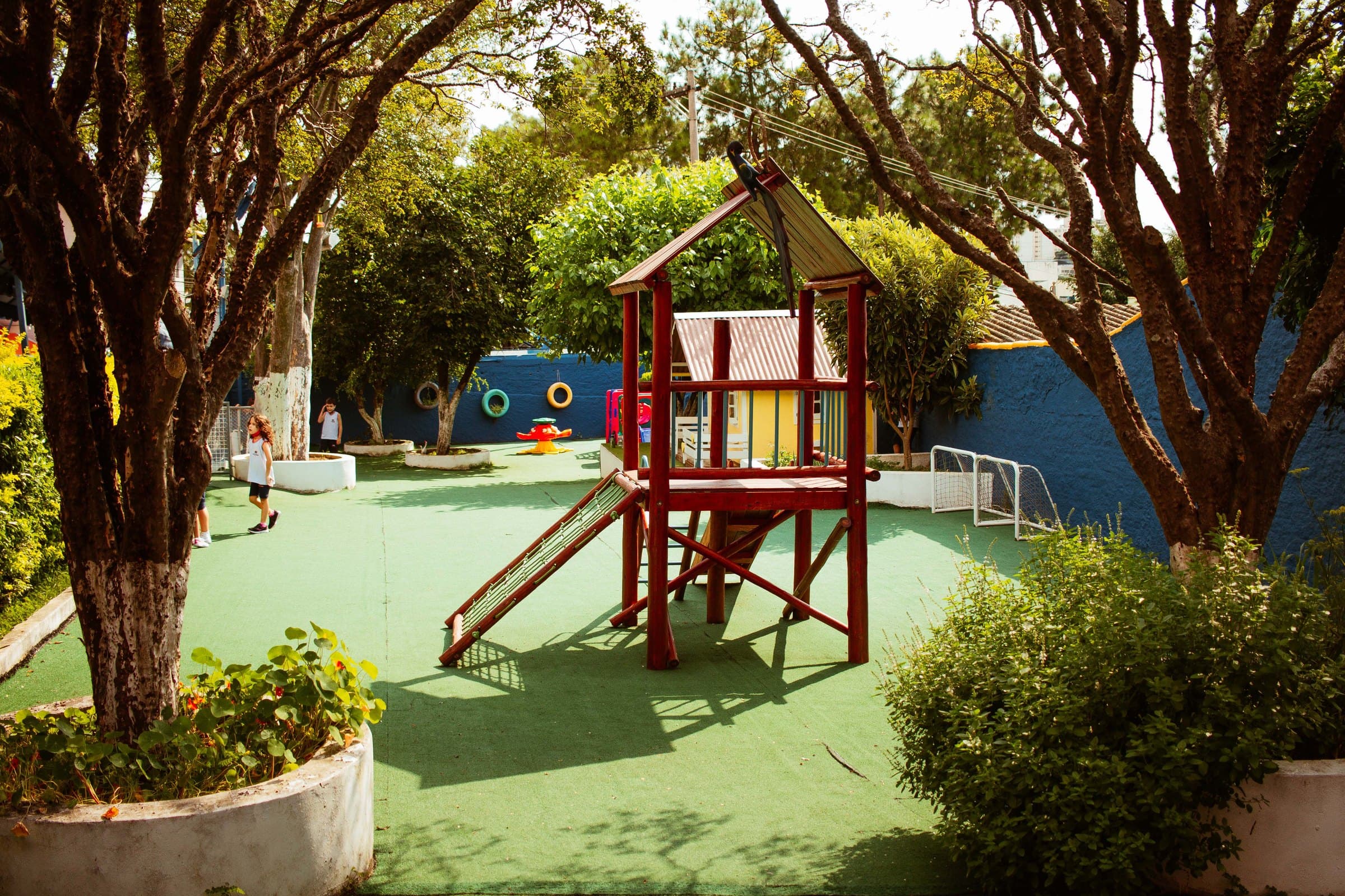Playground do Colégio Jaguaré à sombra de uma árvore, com escorregador de madeira