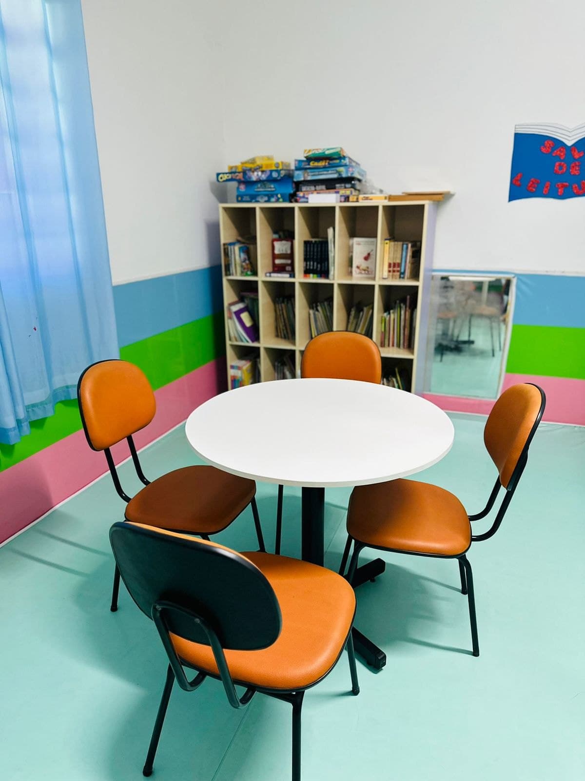 Cantinho de leitura com mesa redonda e cadeiras laranja no Colégio Jaguaré