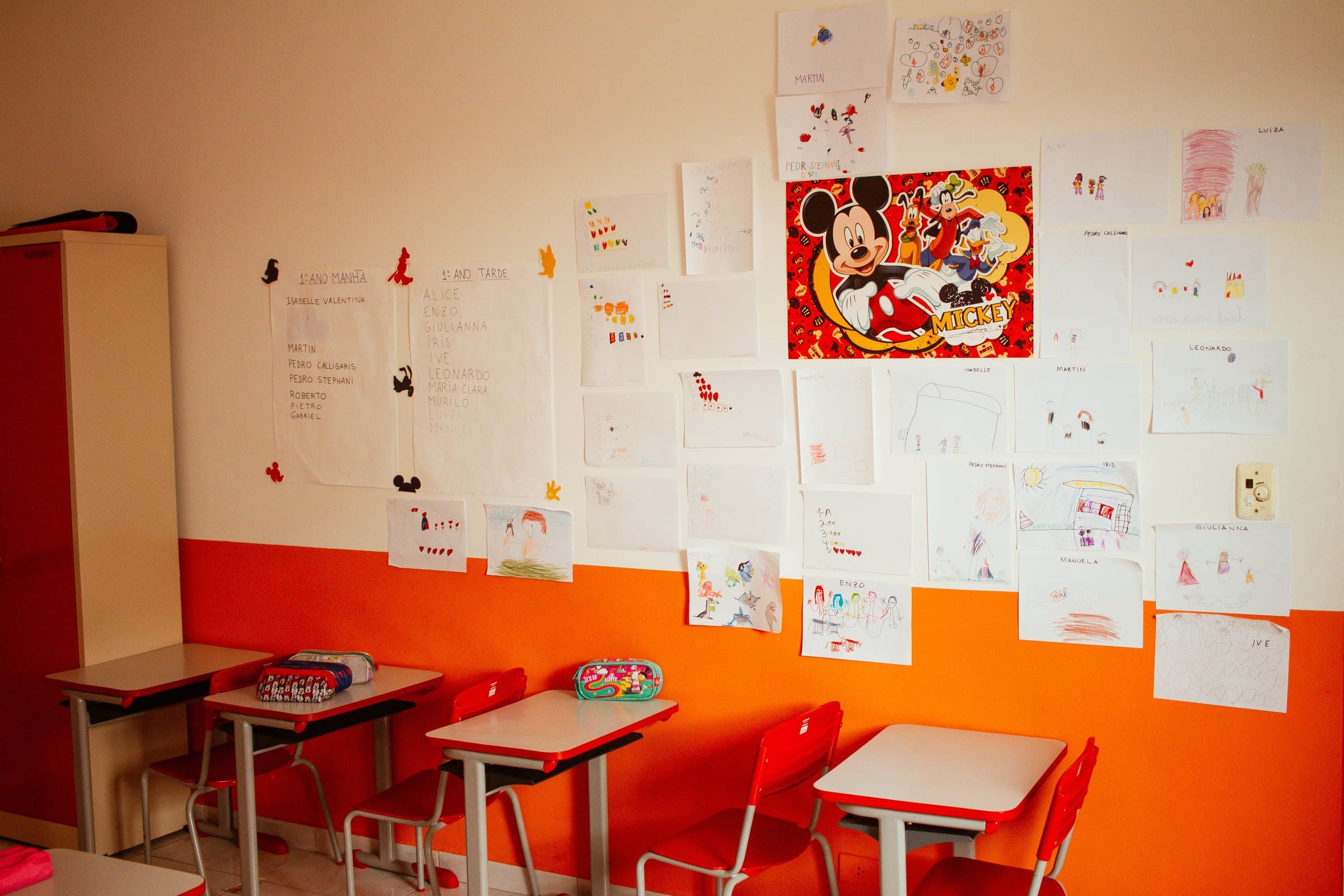 Sala de aula do Colégio Jaguaré com desenhos dos alunos na parede e mesas laranja